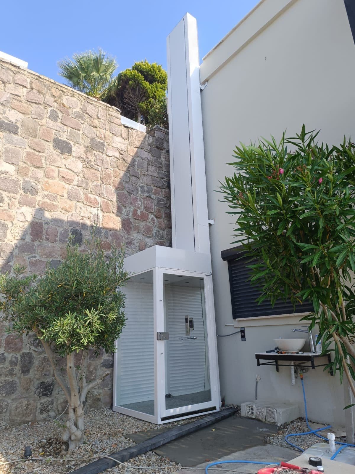 Uzar Lift dış mekân engelli asansörü — villa bahçesine kurulmuş cam kabinli platform lift