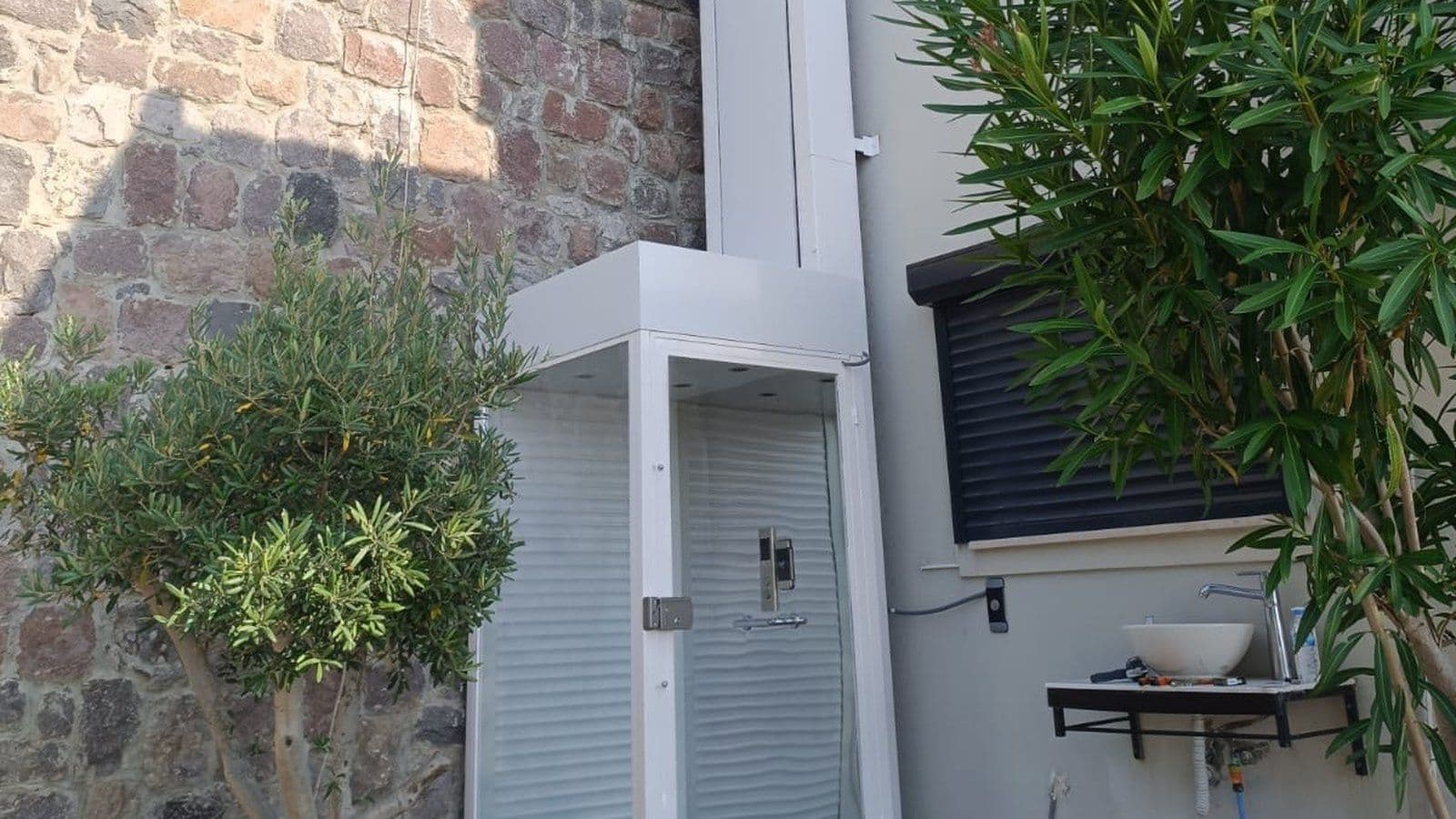 Uzar Lift dış mekân engelli asansörü — villa bahçesine kurulmuş cam kabinli platform lift
